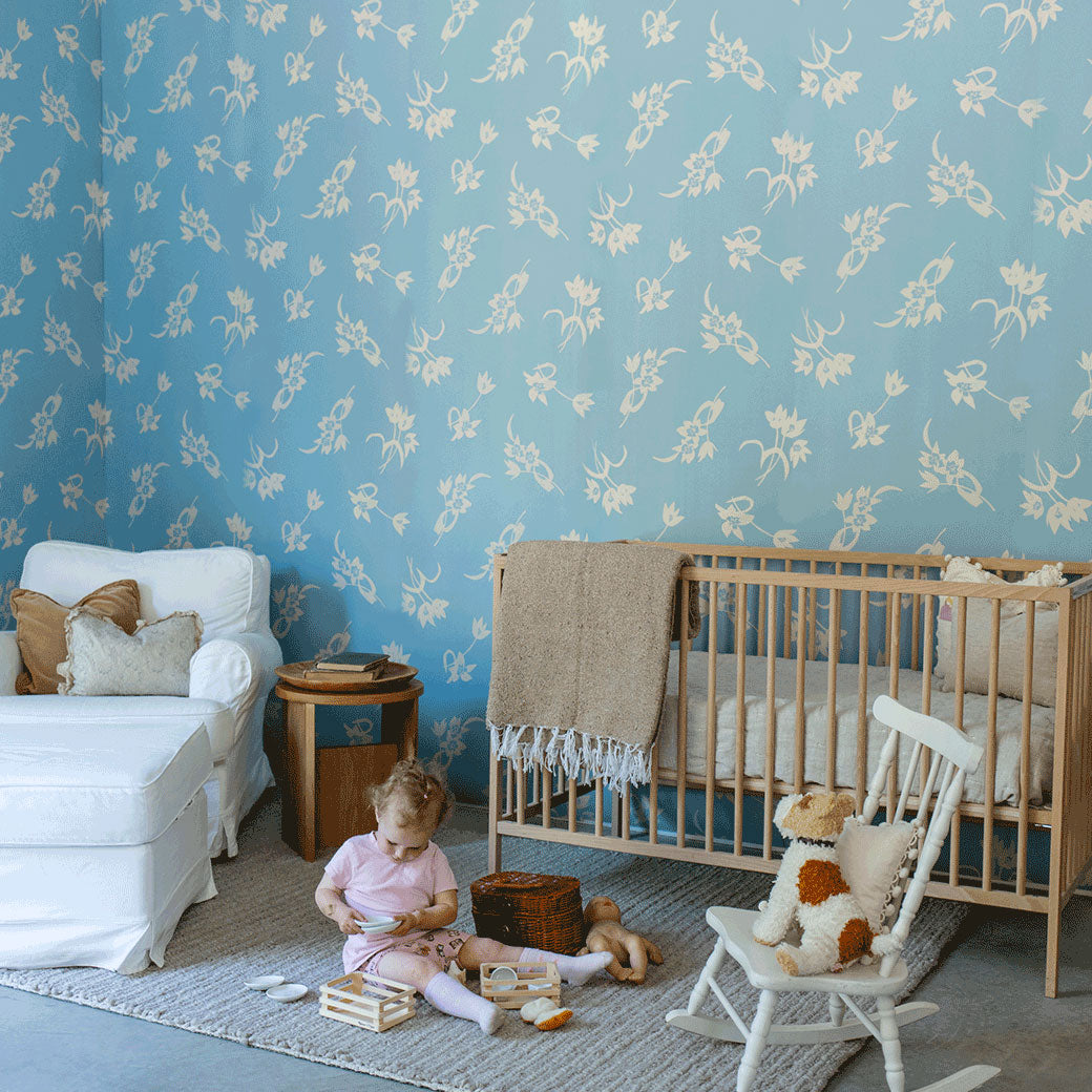 A child sitting on the floor playing next to a crib in a room furnished with Anewall After The Rain Floral Mural