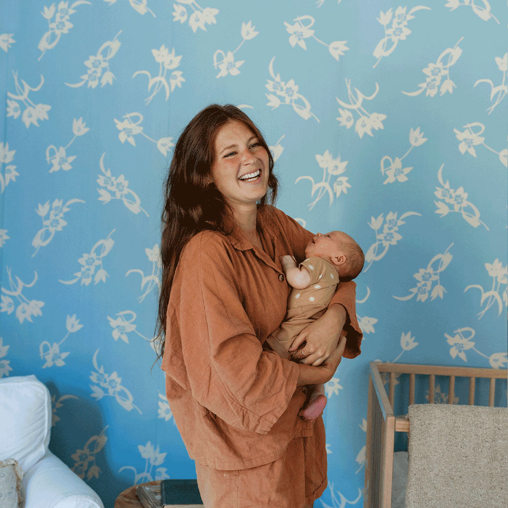 A mother laughing and holding a baby nest to the Anewall After The Rain Floral Mural