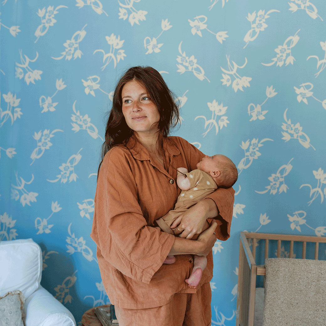 A mother standing and holding a baby next to the Anewall After The Rain Floral Mural