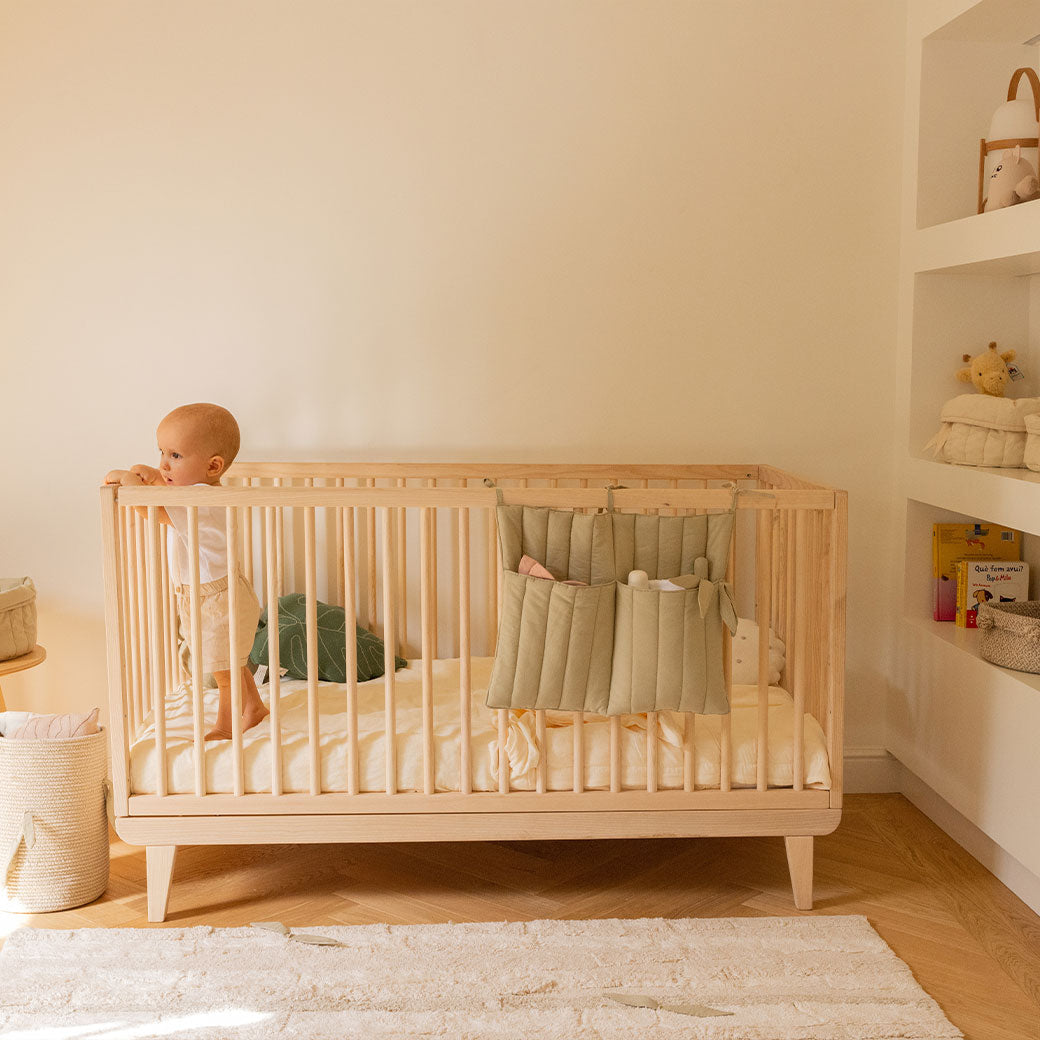 Lifestyle view of Lorena Canals Benjamin Pocket Hanger on a crib with a baby inside  in -- Color_Olive