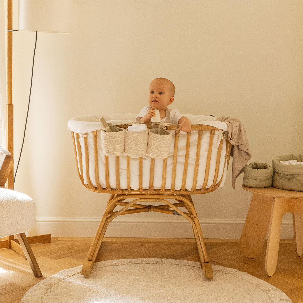 Lifestyle view of baby in a crib equipped with the Lorena Canals Bobby Crib Basket in -- Color_Vanilla