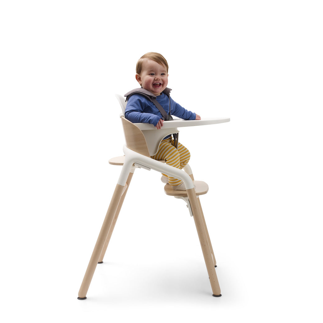 Side view of child sitting in aBugaboo Giraffe High Chair with tray in --Color_Neutral Wood / White
