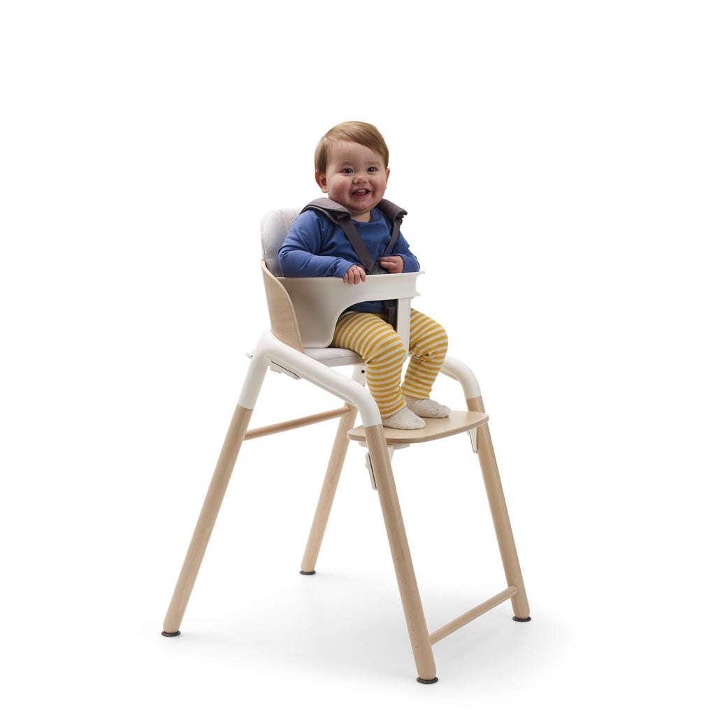 A child sitting in a Bugaboo Giraffe High Chair in --Color_Neutral Wood / White