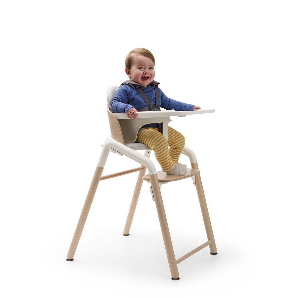 Child sitting in a Bugaboo Giraffe High Chair with tray in --Color_Neutral Wood / White
