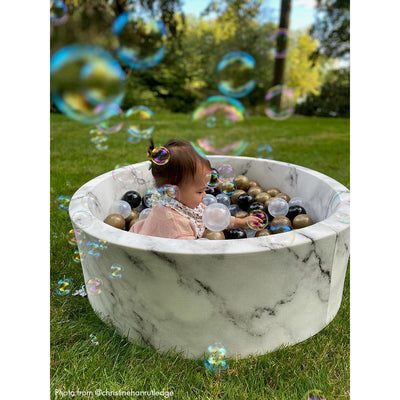 Baby sitting in marble colored ball pit with bubbles in the air -- Lifestyle