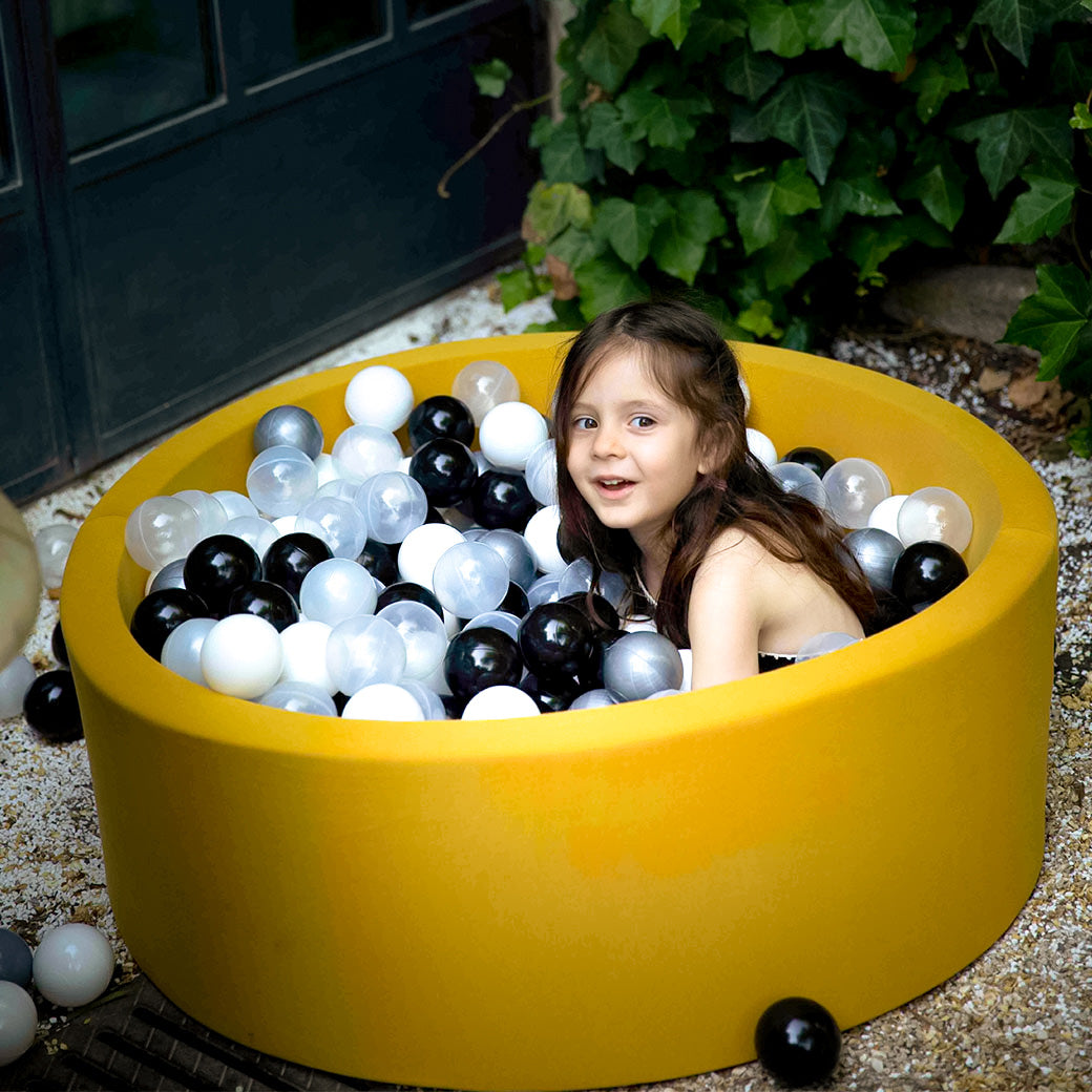 girl playing in mustard colored ball pit -- Lifestyle