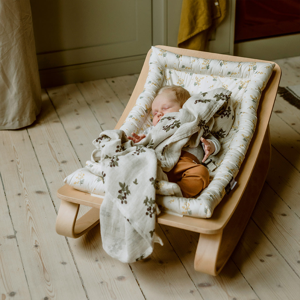 Front view of the baby sleeping in the Charlie Crane LEVO Baby Rocker in -- Color_Garbo And Friends Mimosa _ Beech