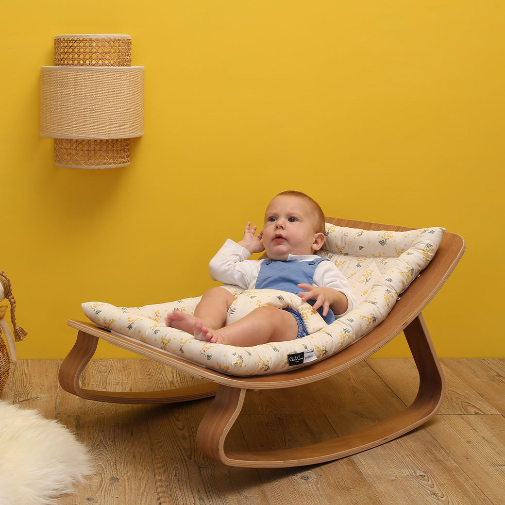 Baby laying down on the Charlie Crane LEVO Baby Rocker in -- Color_Garbo And Friends Mimosa _ Walnut
