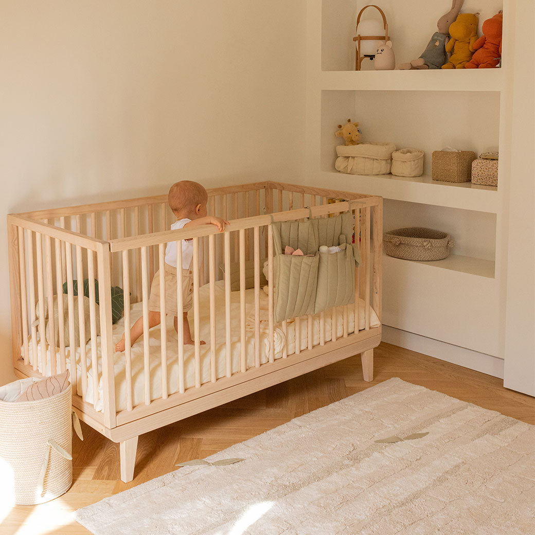 Lorena Canals Bamboo Forest Washable Rug in a room next to a crib with a baby inside 