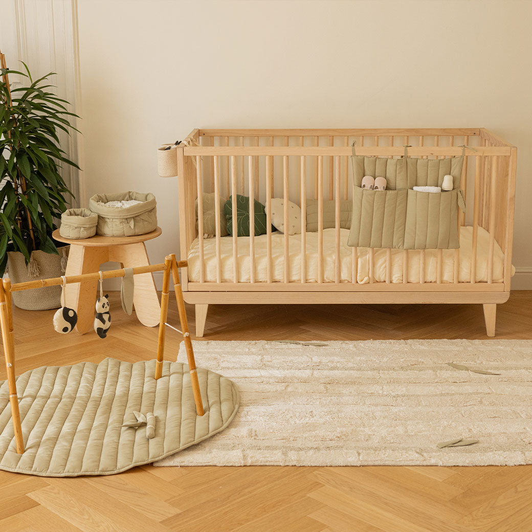 Lorena Canals Products Bamboo Leaf Playmat on a rug next to a crib 