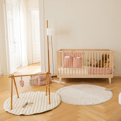 Lifestyle view of the back side of Lorena Canals Products Bamboo Leaf Playmat next to a crib