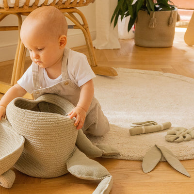A baby playing with a basket on the Lorena Canals Bamboo Leaf Washable Rug