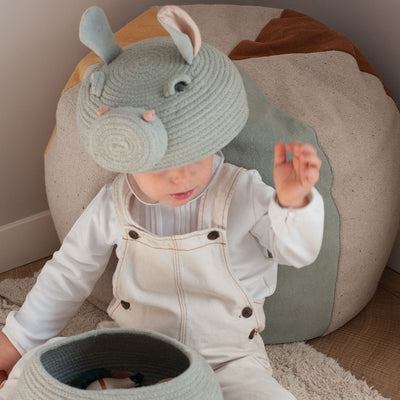 A child playing with the Lorena Canals Henry the Hippo Basket with the top on his head