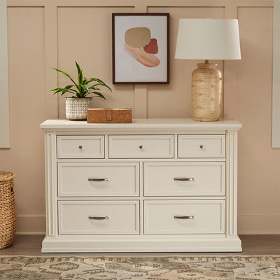 Namesake's Durham 7-Drawer Assembled Dresser in a tan room with a lamp and plant on it in -- Color_Warm White