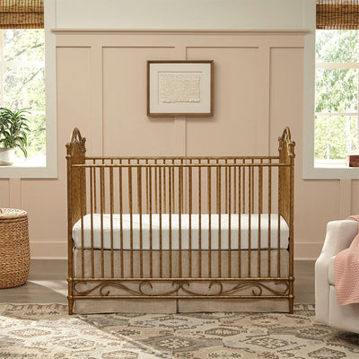 Namesake's Camellia 3-in-1 Convertible Crib next to a recliner and basket  in -- Color_Vintage Gold