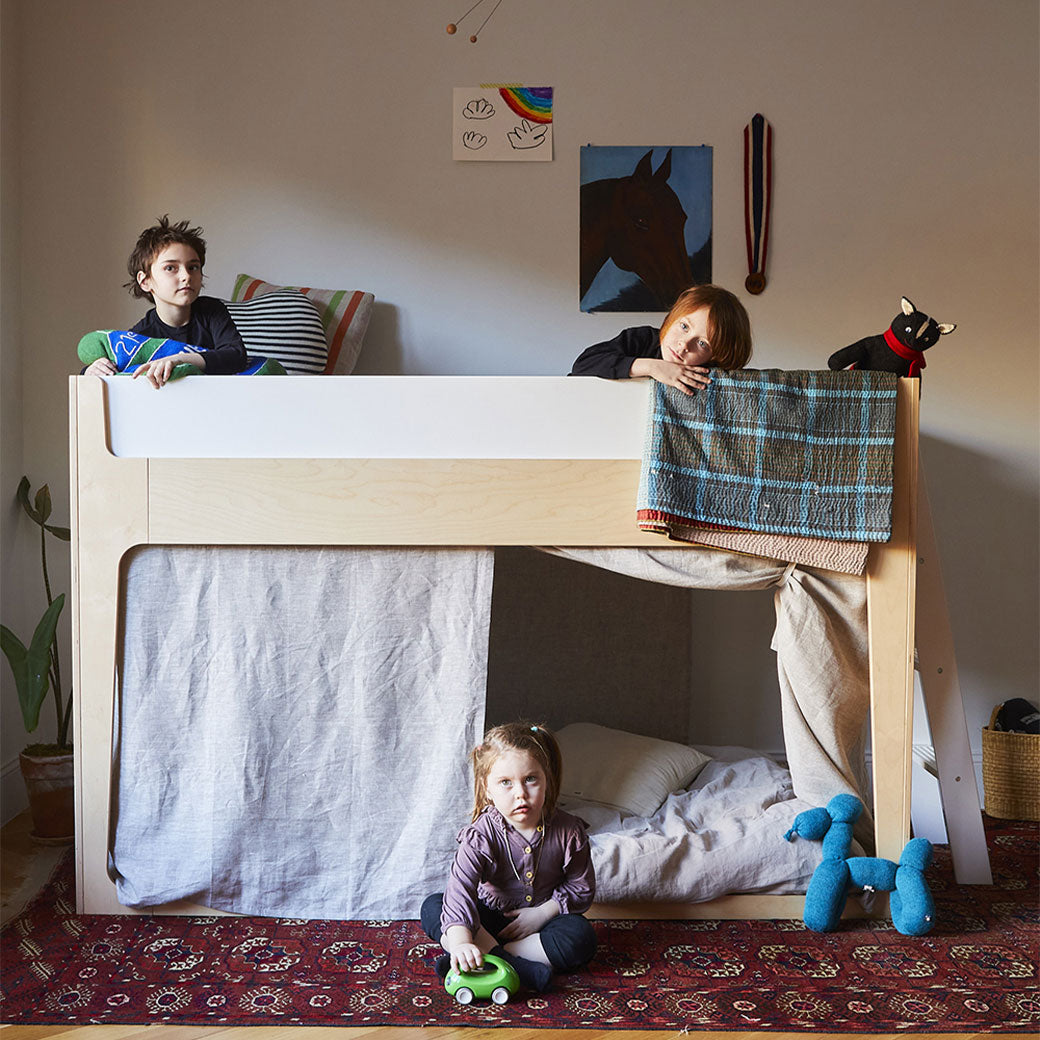 Lifestyle view of Oeuf Perch Nest Bed with two kids on top, and one child on the floor playing