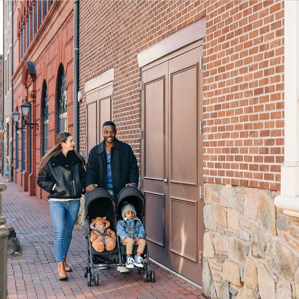 Mother and father walking on the street with kids in UPPAbaby G Link V2 Stroller in --Color_Jake