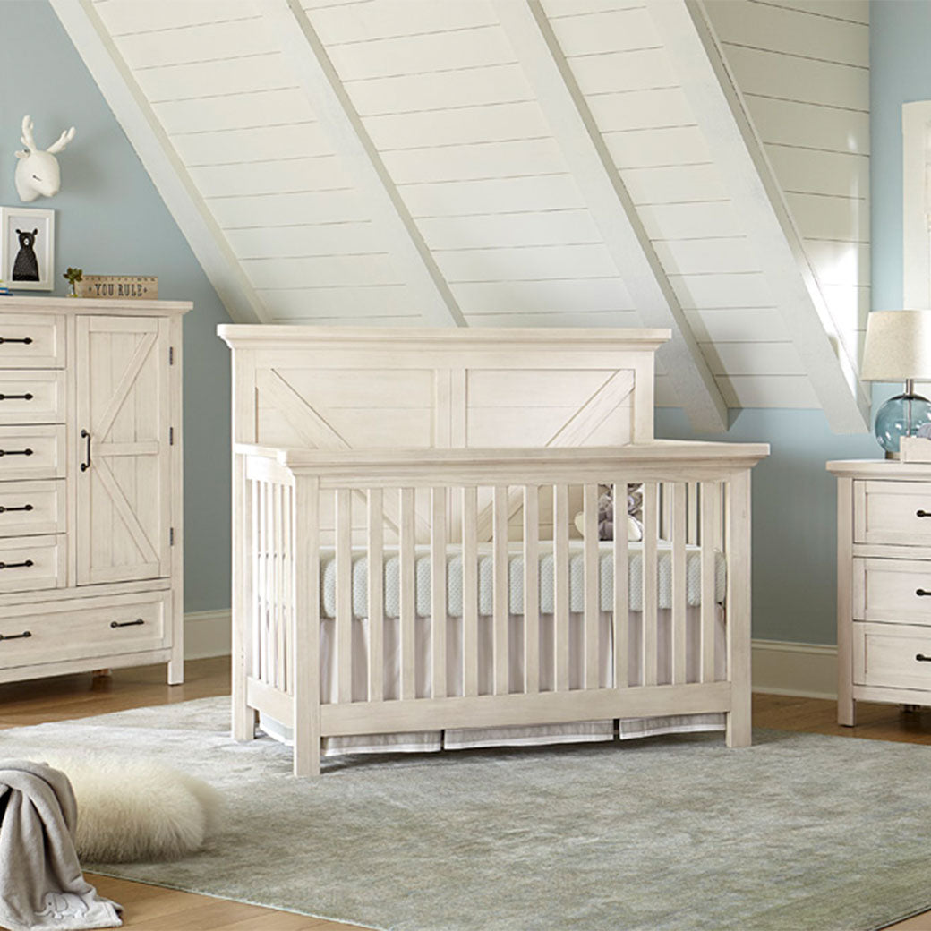 Westwood Design Westfield Convertible Crib in a room next to a dresser  in -- Color_Brushed White